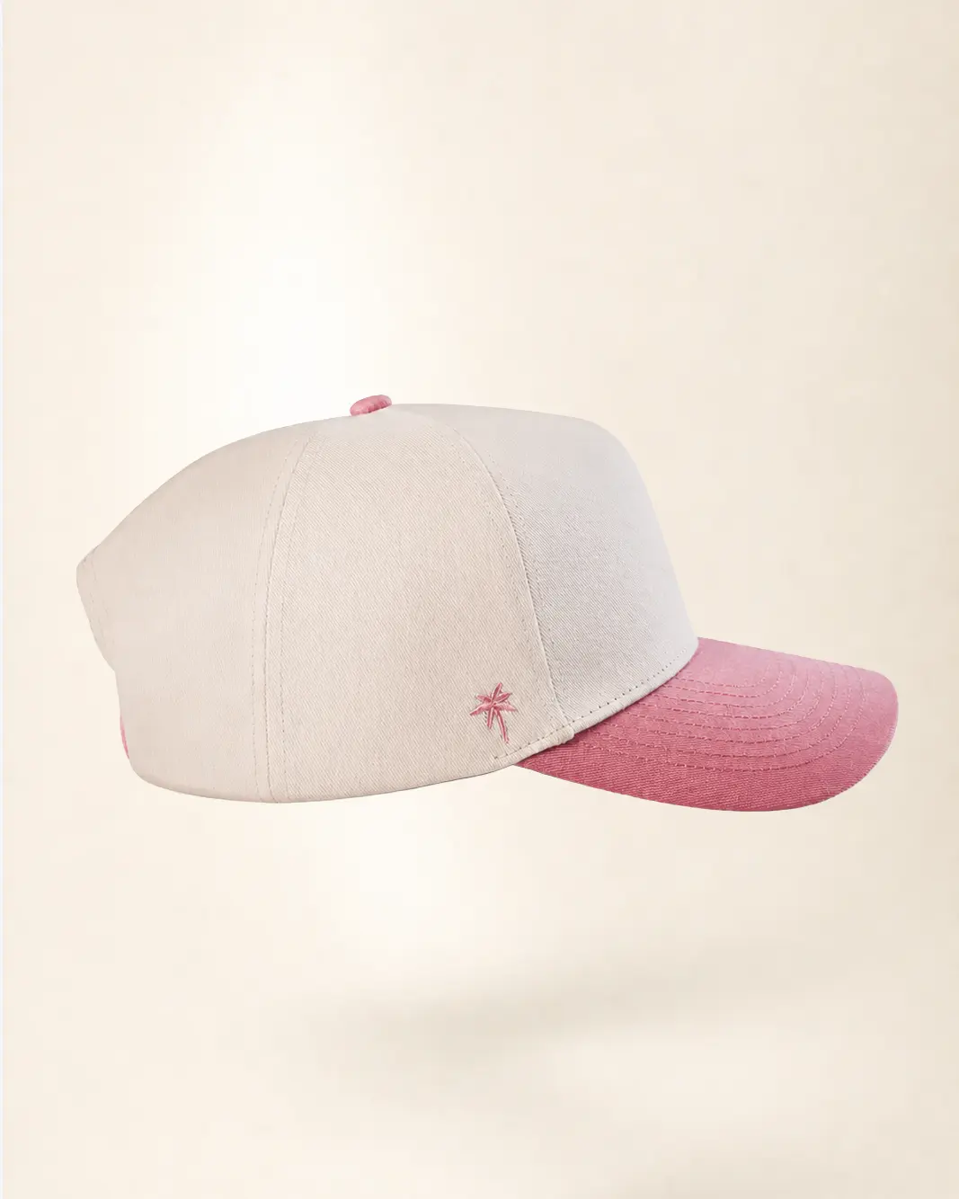A baseball cap with a light beige crown and a dusty pink brim, featuring a small embroidered pink star logo on the side.