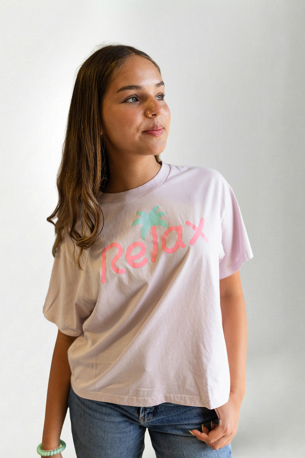 Person wearing a light pink t-shirt with 'Relax' printed on it against a plain background