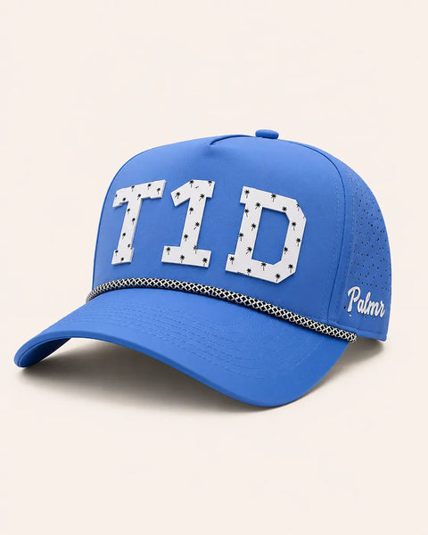 The T1D Signature Hat (Blue): blue rope snapback with T1D in white palm-print letters, black and white rope on the brim, Palmr script on the side.