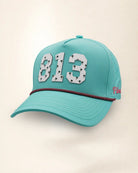 The 813 Signature Hat (Teal), three-quarter view: white raised 813 with small palm print on a teal rope snapback, pink and black rope, pink Palmr script.