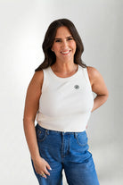 Woman wearing a white tank top and blue jeans against a plain background