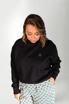 Woman wearing a black sweatshirt and patterned pants on a plain background