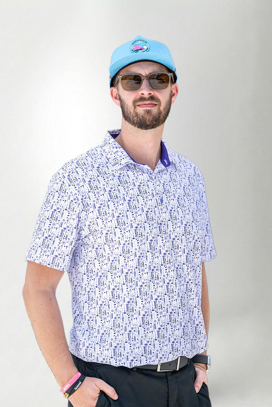 Man wearing a patterned shirt, sunglasses, and a blue cap against a plain background