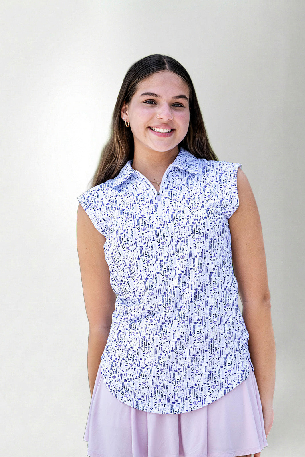 Woman wearing a sleeveless patterned top and light purple skirt against a plain background