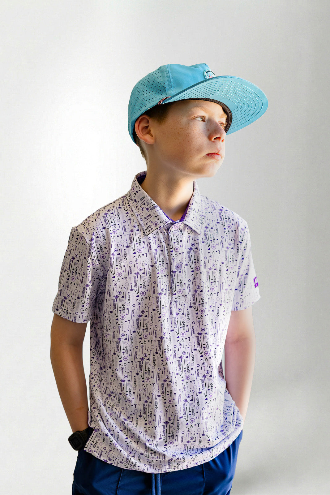Child wearing a patterned shirt and blue cap against a plain background