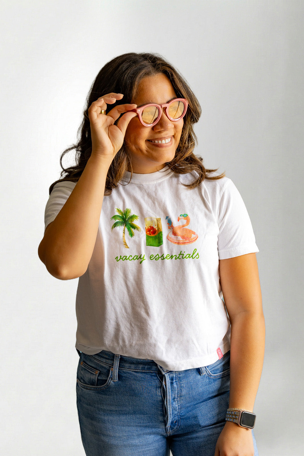Person wearing a white t-shirt with a colorful graphic and text, holding glasses.