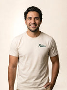 A smiling man wearing a light beige crewneck t-shirt with the brand name 'Palmr' printed in dark green script on the left chest, set against a plain beige background.